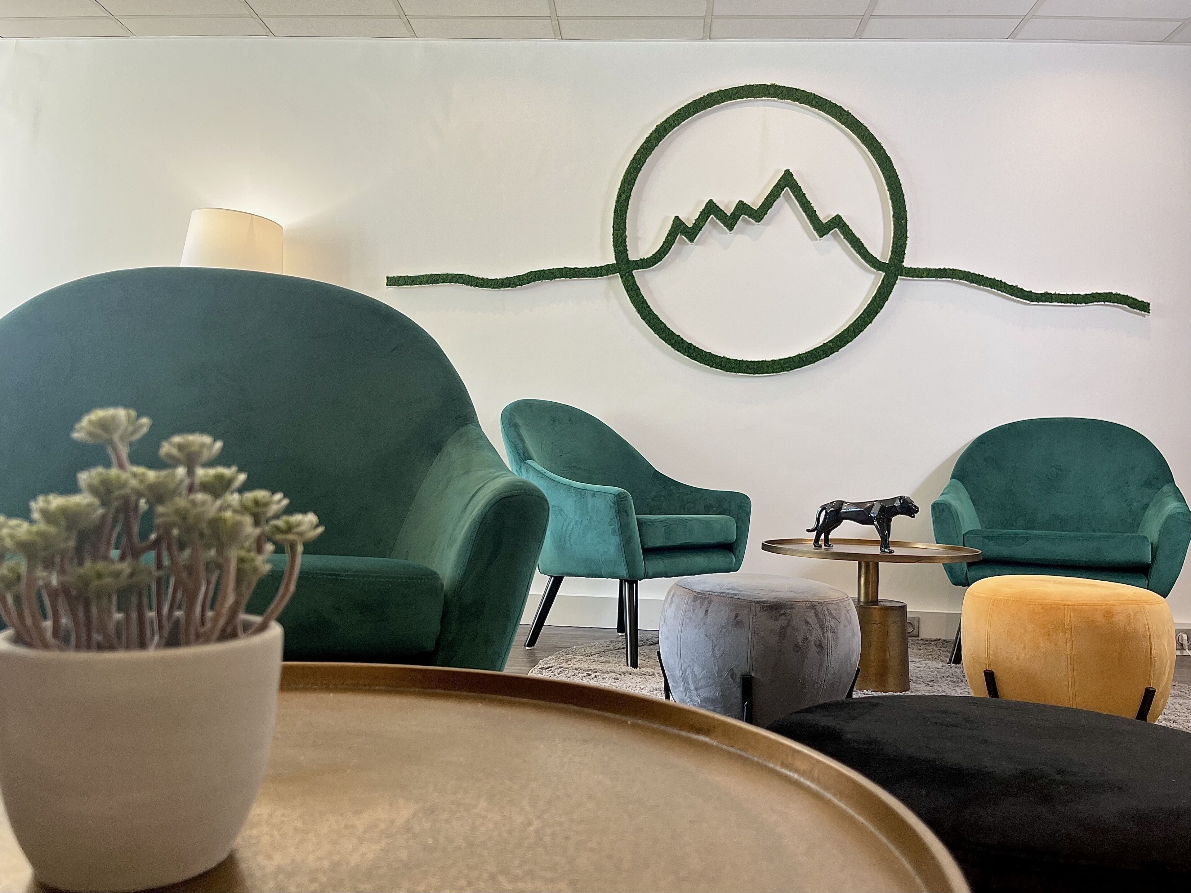 Un espacio lounge moderno con sillas color turquesa, una mesa redonda y un elemento decorativo en la pared.