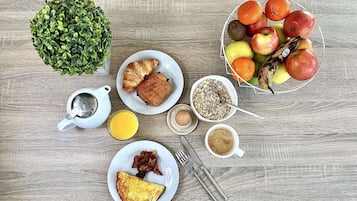 A breakfast table with croissants, fruits, a teapot, a glass of orange juice, and a small plant.