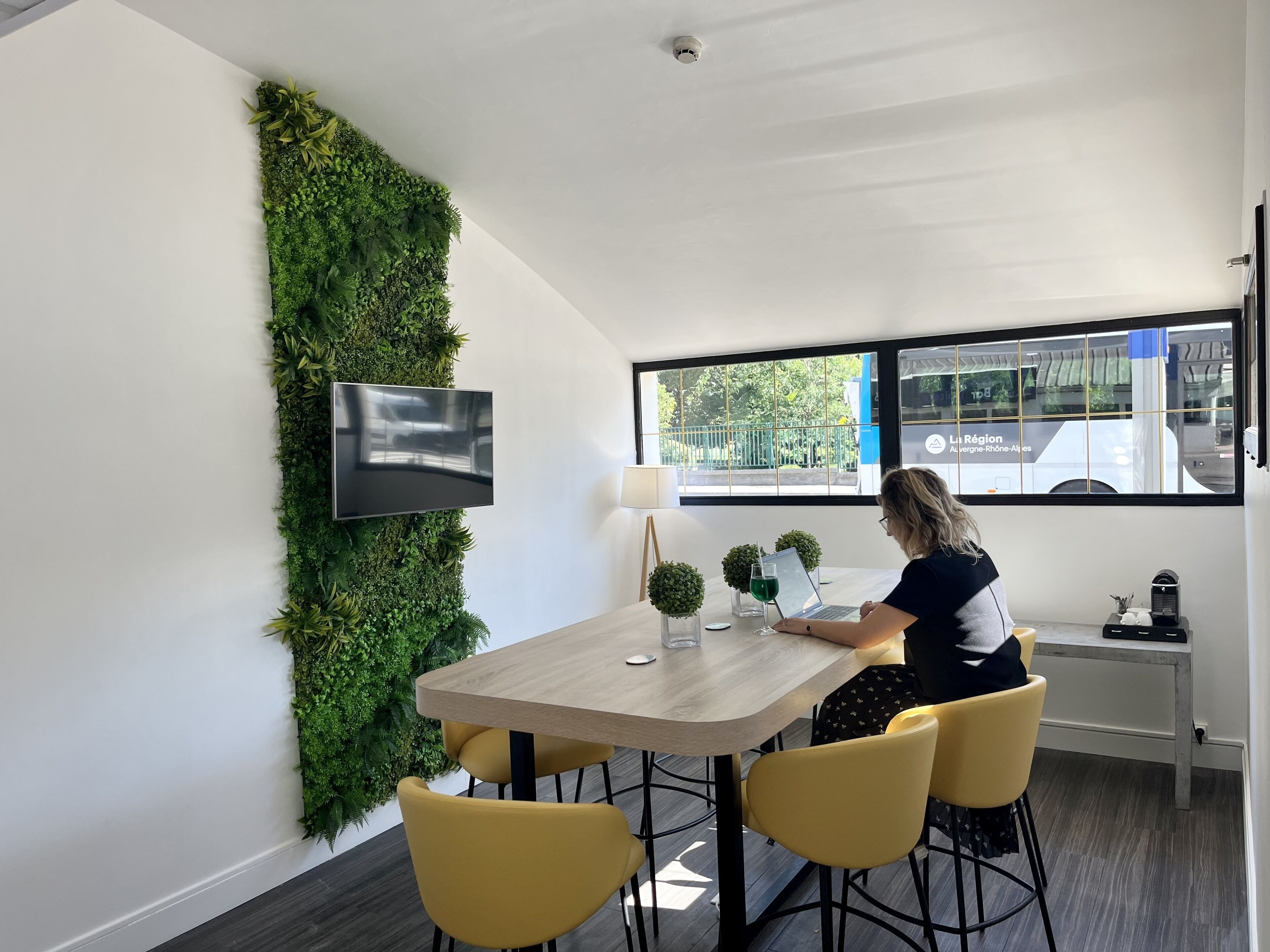 A modern room with a wooden table, yellow chairs, a flat-screen TV, and a green wall.