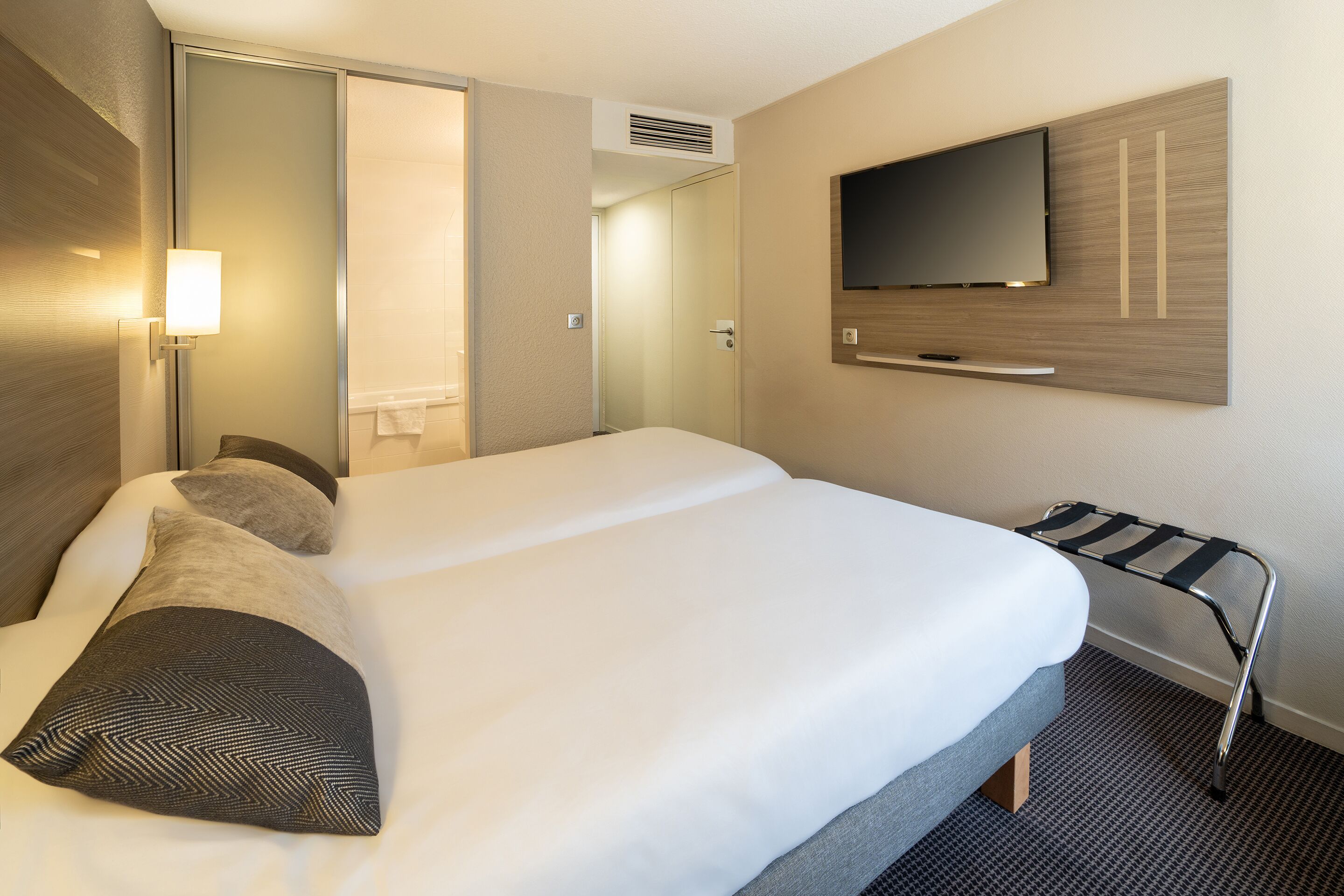 Una habitación de hotel con una cama grande, un televisor montado en la pared y una mesita de noche.