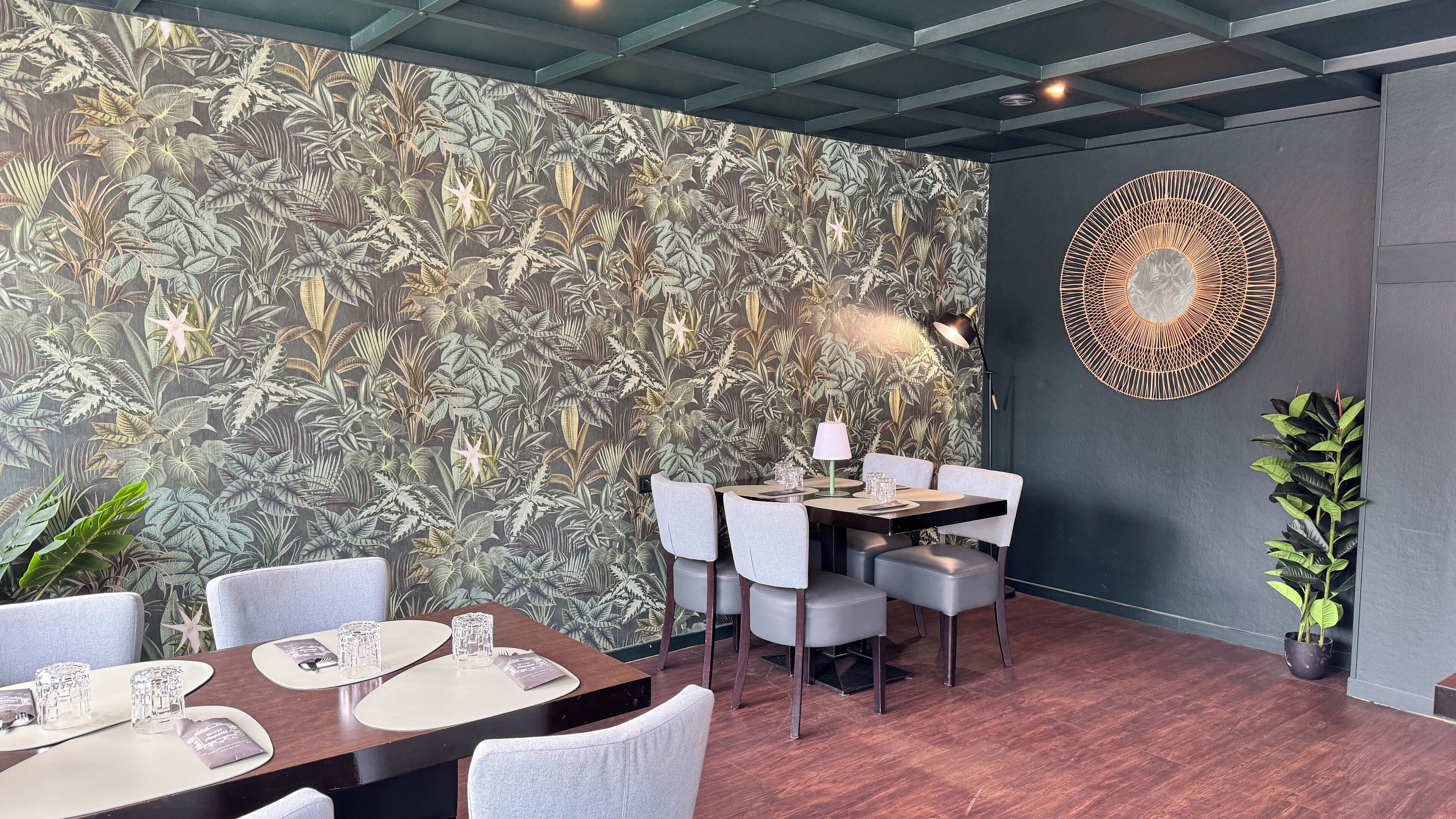 A dining area with a tropical leaf-patterned wall, a round table with chairs, and a decorative wall piece.