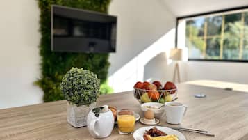 A breakfast setup with a croissant, omelette, and fruit bowl on a wooden table, a pitcher, a glass of orange juice, and a cup of coffee.