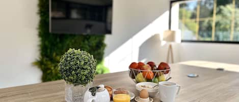 A breakfast setup with a croissant, omelette, and fruit bowl on a wooden table, a pitcher, a glass of orange juice, and a cup of coffee.