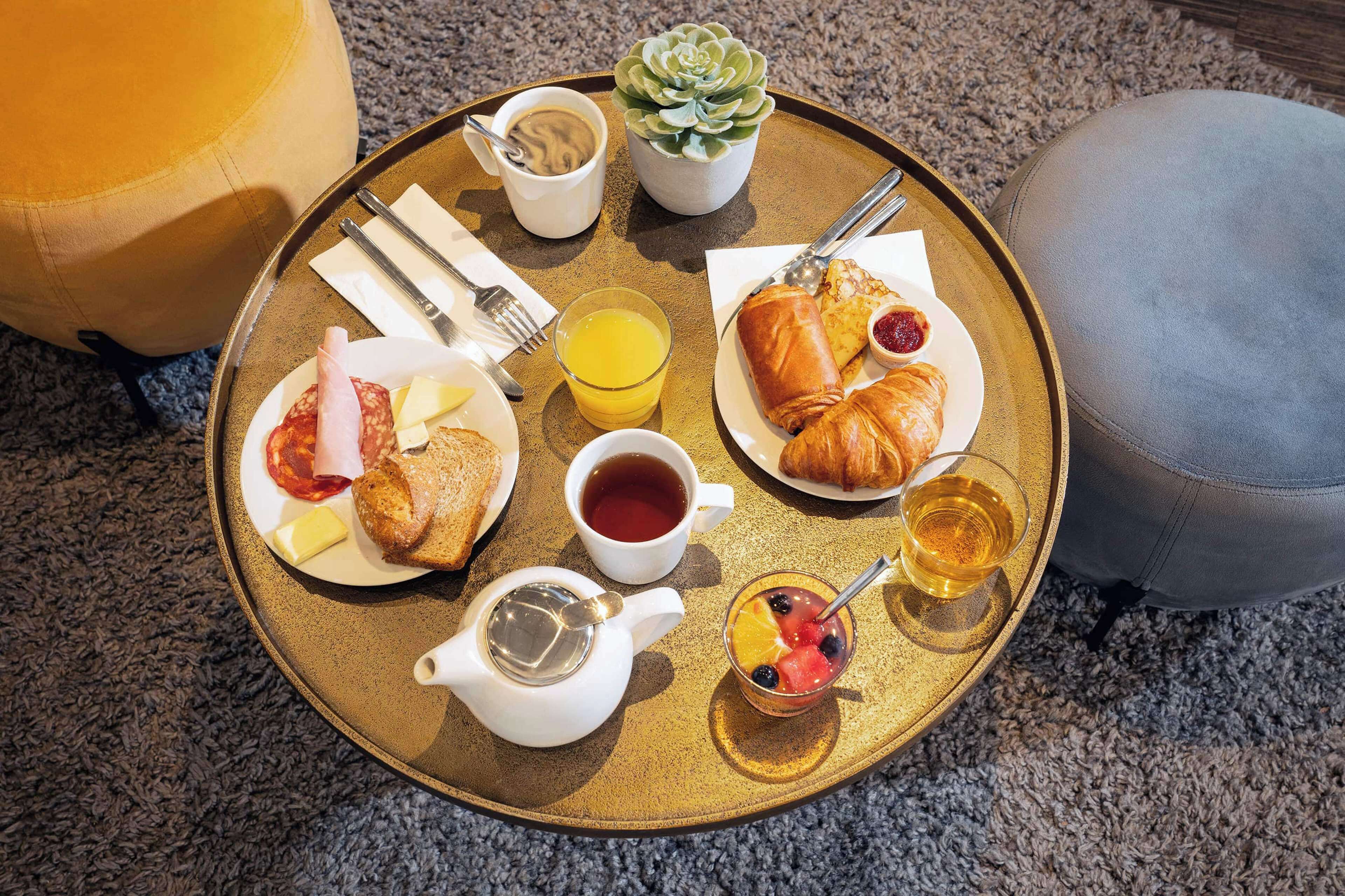Ein Frühstückswagen mit Croissants, Käse, Schinken, Toast, Obst, Tee und Saft.