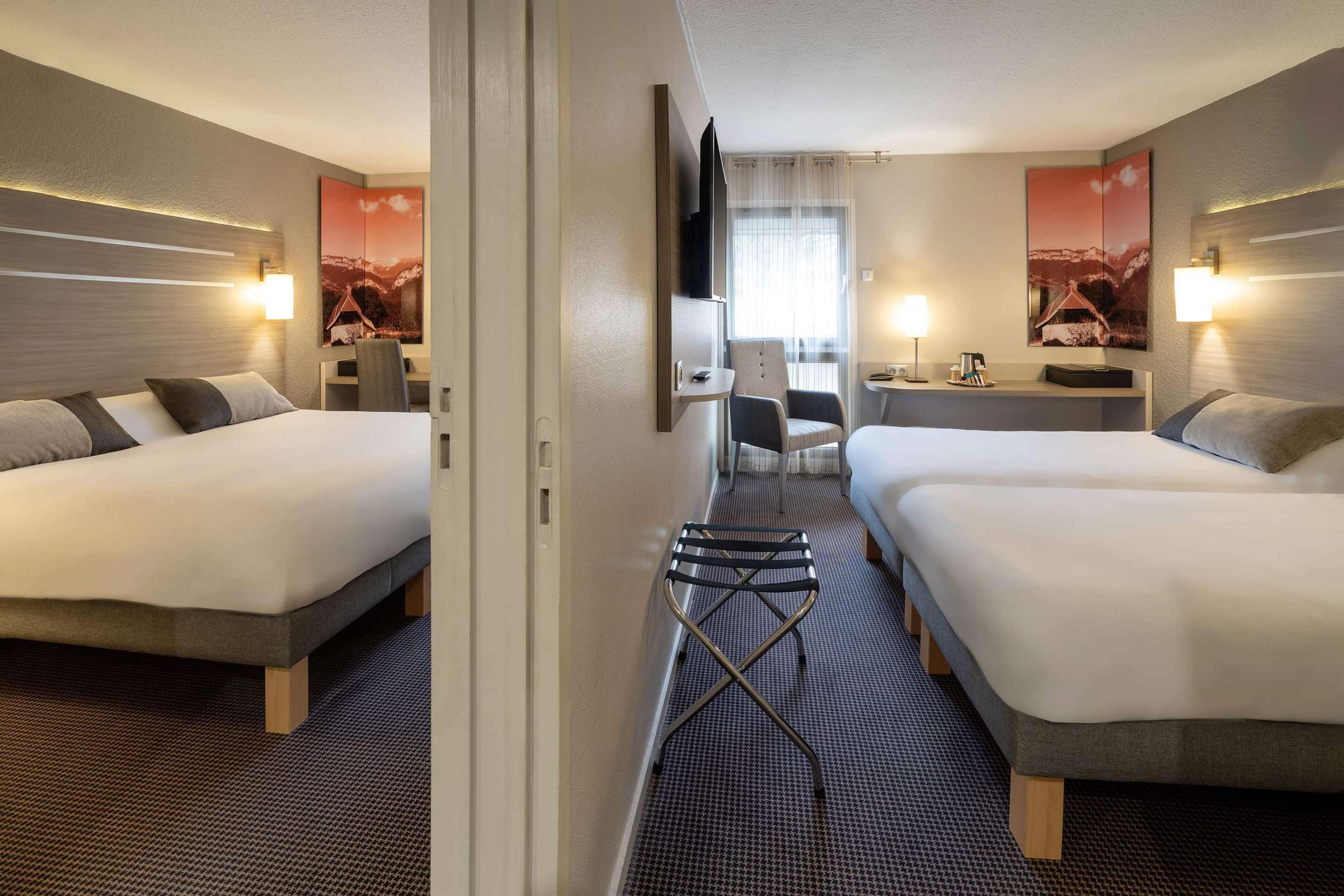 Une chambre d’hôtel avec deux lits, un bureau, une chaise, une télévision et des œuvres d’art accrochées aux murs.