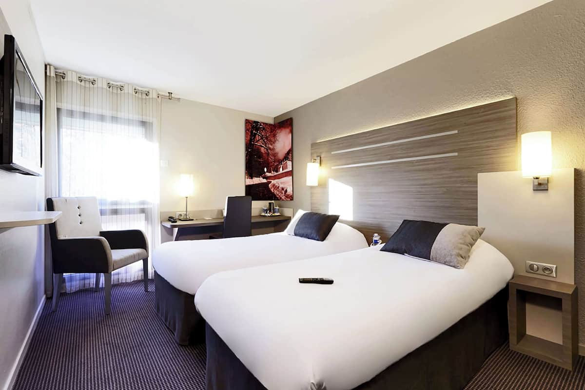 Une chambre d’hôtel avec deux lits, un bureau, une chaise et un téléviseur.