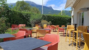 An outdoor seating area with tables and chairs, surrounded by greenery and a mountain view.