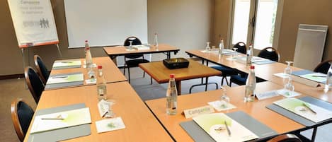 Une salle de conférence équipée de plusieurs tables, de porte-noms, de bouteilles d’eau et d’un écran de projection.