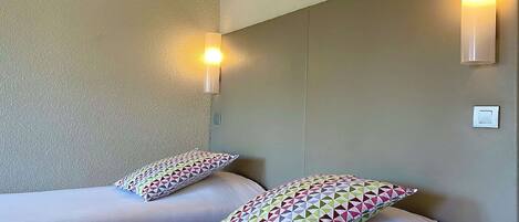 Habitación de hotel con dos camas, cada una con almohada estampada, una lámpara de pared y un interruptor de luz.