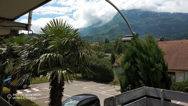 A parking area with a mountain view, a palm tree, and a building with a tiled roof.
