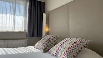 Ein Hotelzimmer mit einem Bett, zwei Kissen, einem Fenster mit Vorhängen und einer Wandleuchte.