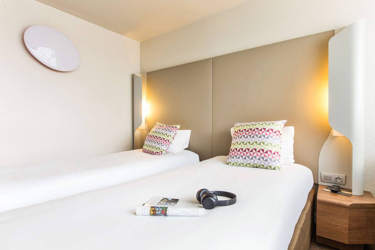 Une chambre d’hôtel avec deux lits, chacun muni d’un oreiller et d’une lampe de chevet. Un casque audio est posé sur l’un des lits et un livre sur l’autre.
