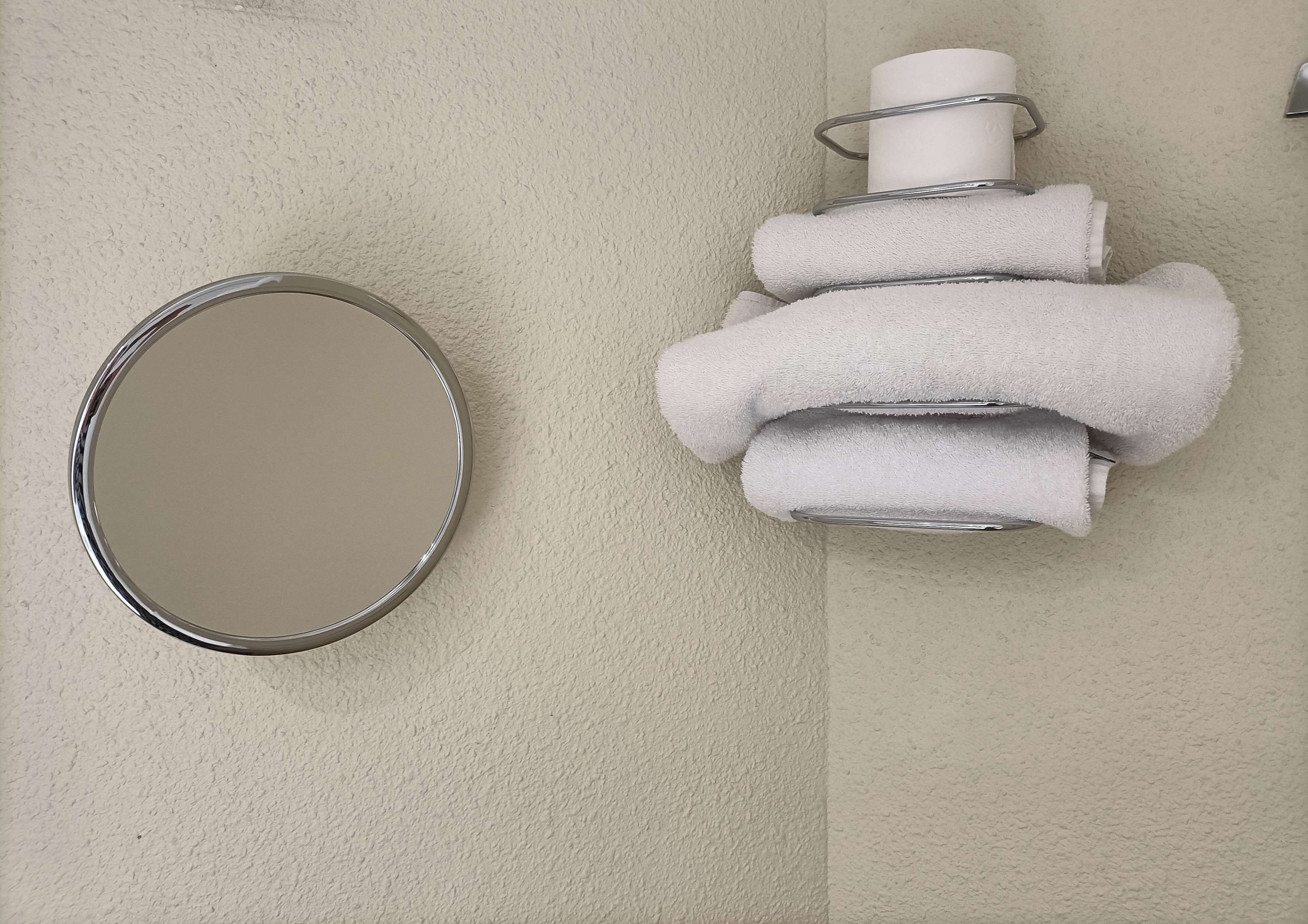 A bathroom with a round mirror and a towel rack with multiple towels.