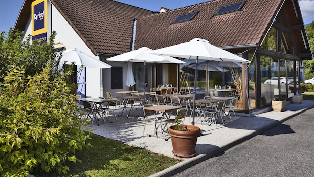 A hotel with outdoor seating, a tiled roof, and a large window.