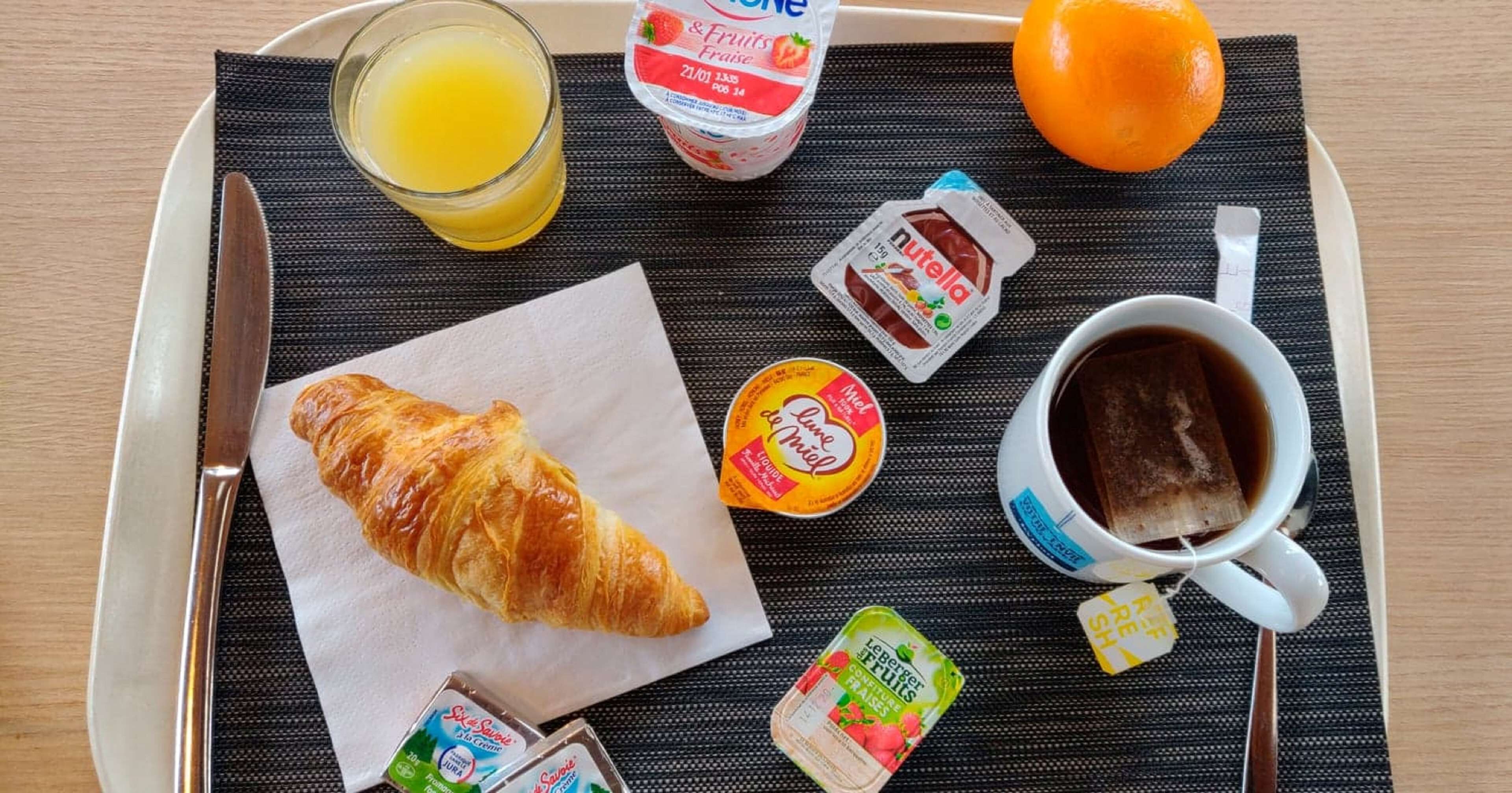 A tray with a croissant, juice, yogurt, Nutella, and coffee.
