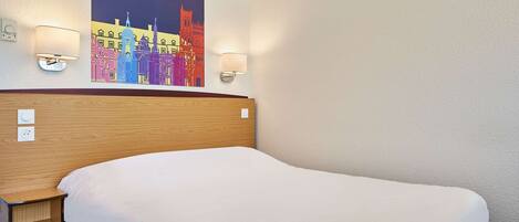 Una habitación de hotel con una cama grande, cabecera de madera, dos lámparas fijadas a la pared y un cuadro de un paisaje urbano colorido sobre la cama.