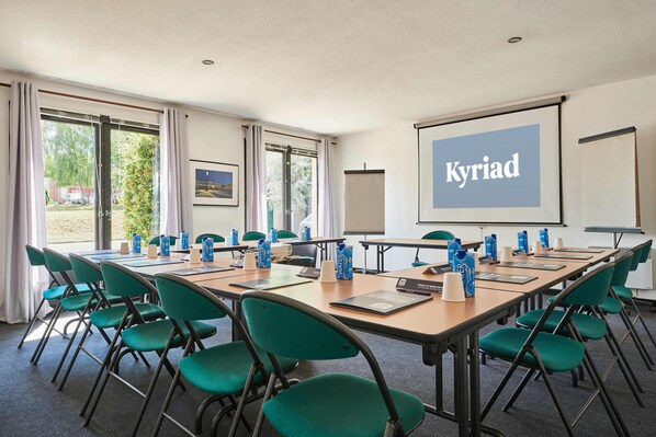 A conference room with a long table, green chairs, water bottles, and a screen displaying "Kyriad". - Kyriad Nancy Ouest - Laxou Zenith (Maxeville)