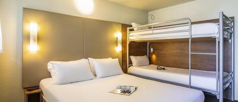 A hotel room with a bunk bed, a bedside table with a remote control, and a magazine on the bed.