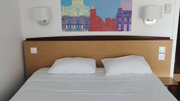A hotel room with a bed, two bedside lamps, and a colorful cityscape painting on the wall.