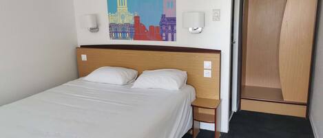 A hotel room with a bed, a nightstand, a wall-mounted air conditioner, and a painting of a cityscape.
