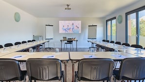 Een vergaderzaal met lange tafels, stoelen, een projectiescherm en een presentatie op de muur.
