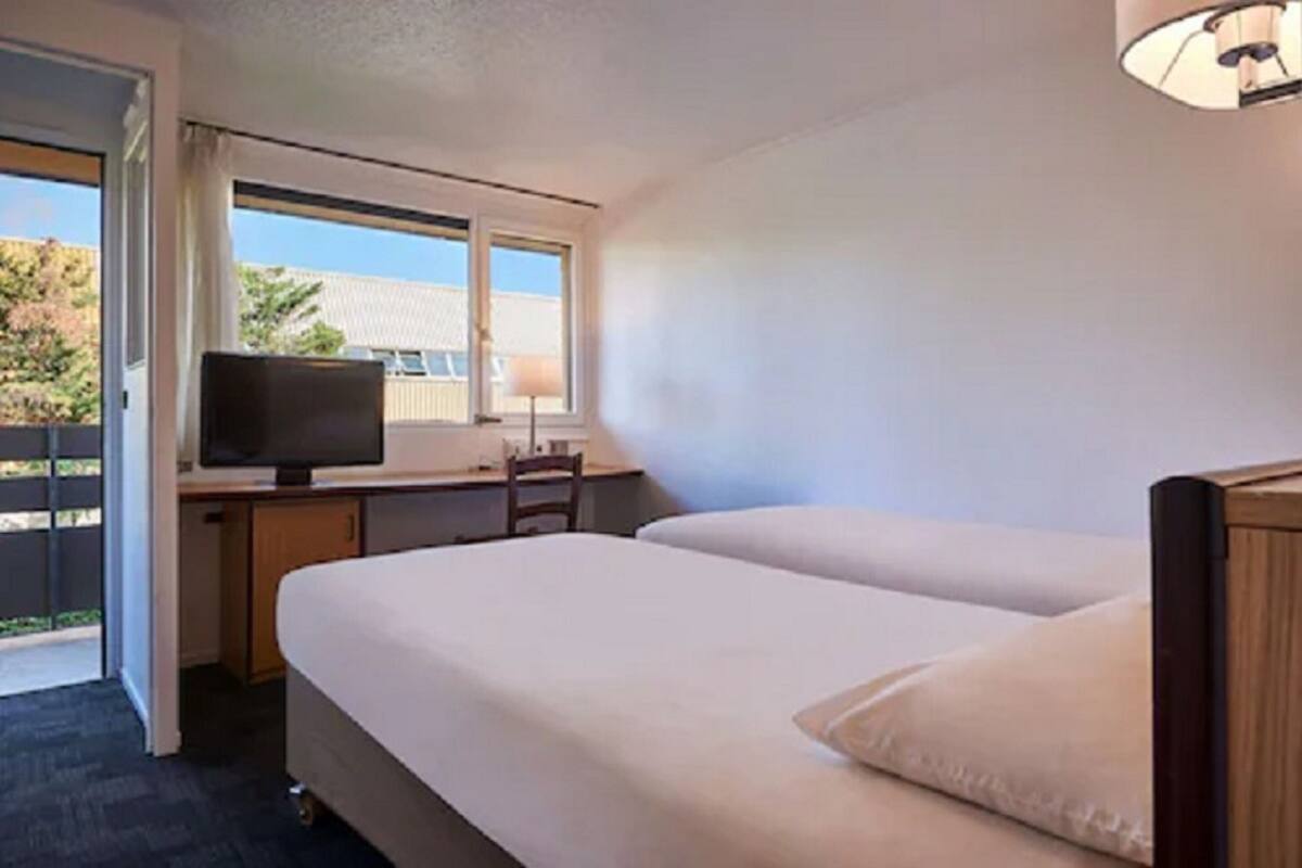 Une chambre d’hôtel équipée d’un lit, d’un bureau avec une télévision et d’une fenêtre donnant sur l’extérieur.