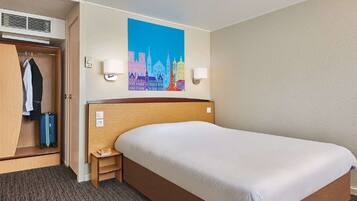 A hotel room with a large bed, a wardrobe, a desk, and a cityscape painting on the wall.