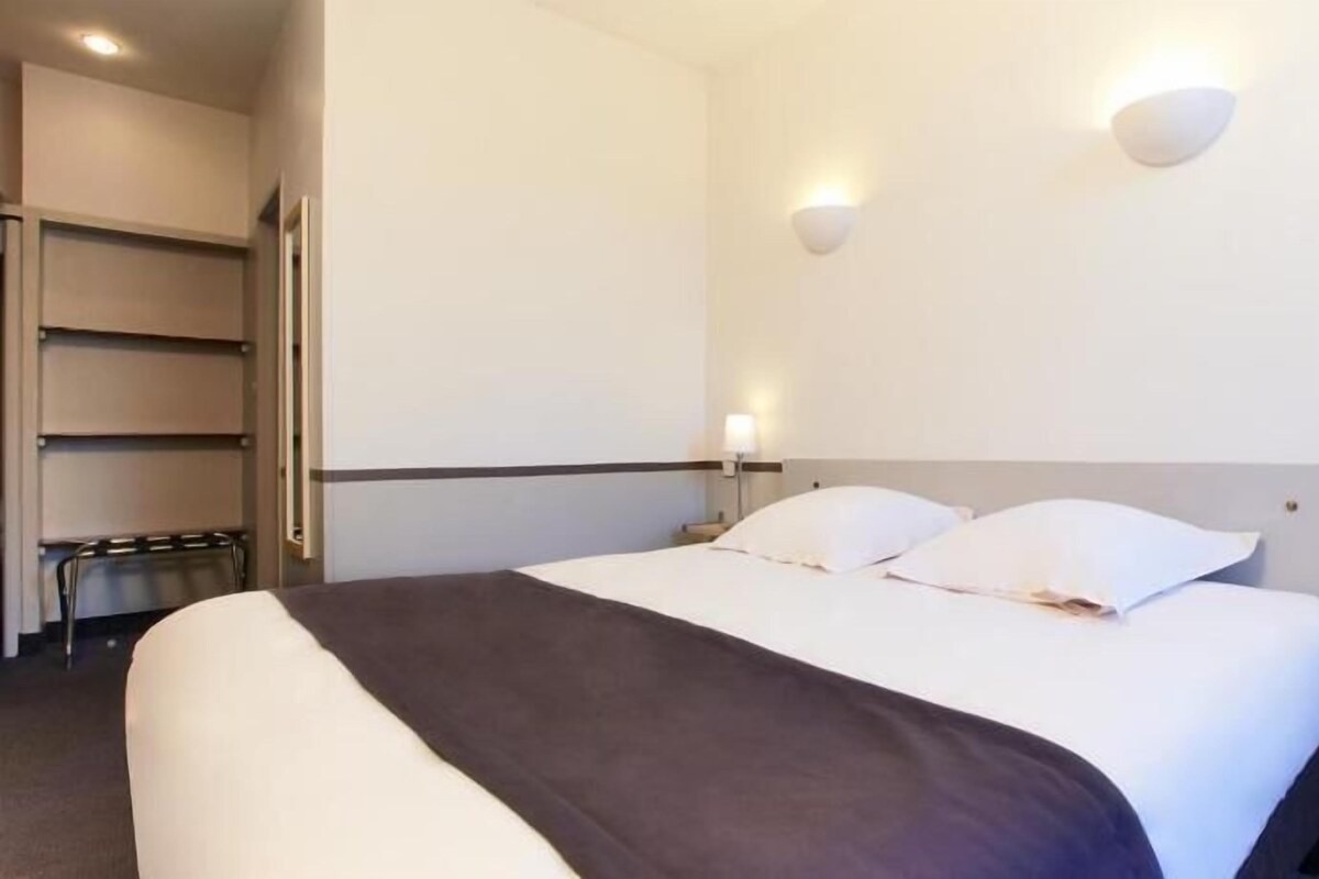Habitación de hotel con cama, lámparas de noche, mesita de noche y estante en la pared.