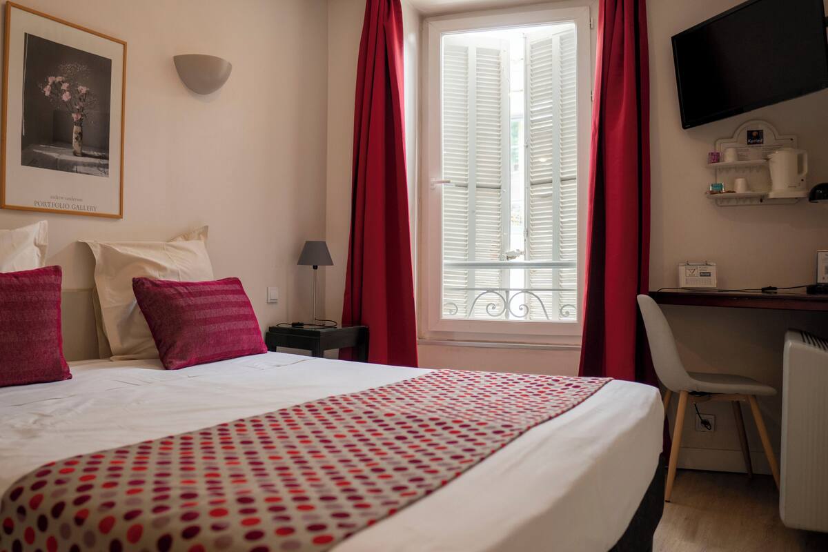 A hotel room with a bed, a desk, a chair, a TV, and a window with curtains.