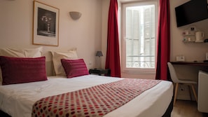 A hotel room with a bed, a desk, a chair, a TV, and a window with curtains.