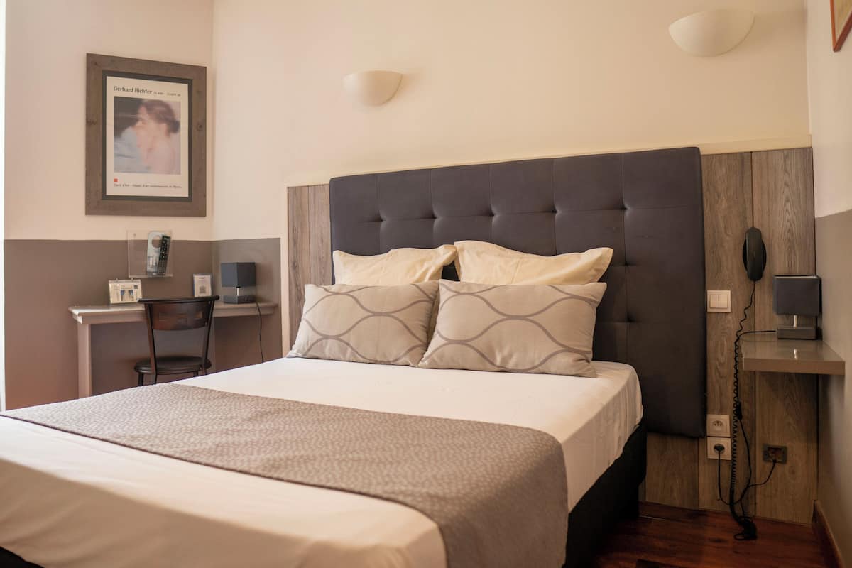 A neatly arranged hotel room with a large bed, a desk, and a chair.