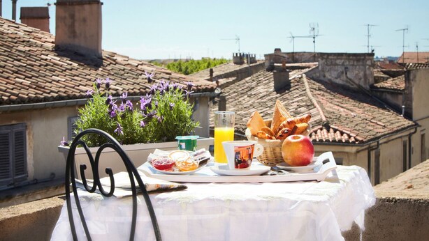 A breakfast setup on a rooftop terrace with a table, chairs, and a variety of food and drink items. - Plazza hôtel (Nîmes)