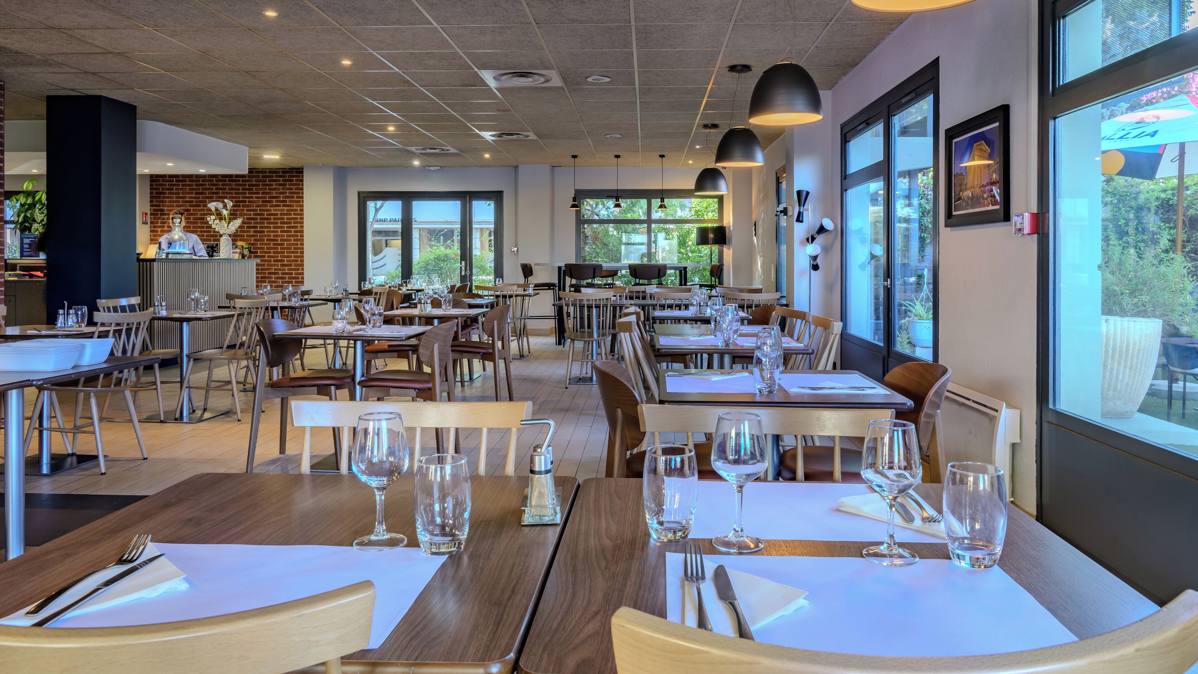 A spacious restaurant with multiple tables and chairs, large windows offering a view of the outdoors, and a modern interior design.