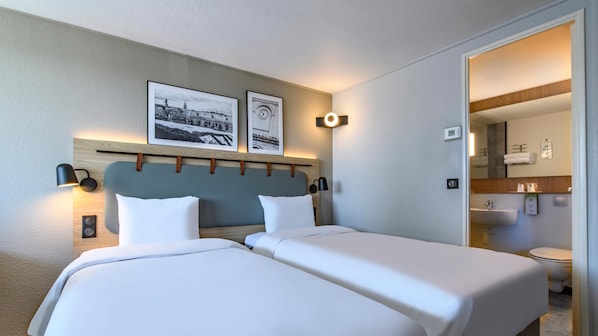 A hotel room with two beds, a wooden headboard, wall-mounted lamps, and framed pictures.