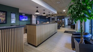 A reception area with a wooden reception desk, a TV screen, and a potted plant. - Campanile PRIME - Nîmes Centre (Nîmes)