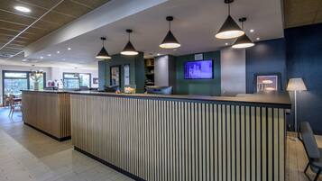 A reception area with a wooden reception desk, pendant lighting, a television screen, and a view of the outdoors.