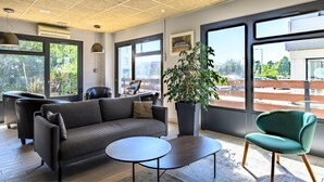 A modern interior with a sofa, a round table, and a chair. There are large windows with a view of the outside. - Campanile PRIME - Nîmes Centre (Nîmes)
