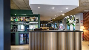 A bar area with shelves of liquor bottles and glasses, a refrigerated display, and a counter with a decorative vase. - Campanile PRIME - Nîmes Centre (Nîmes)