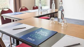 A conference room with a table set for a meeting, including a 'Bien Venue Well Come' welcome card, a bottle, glasses, and a pen on the table.