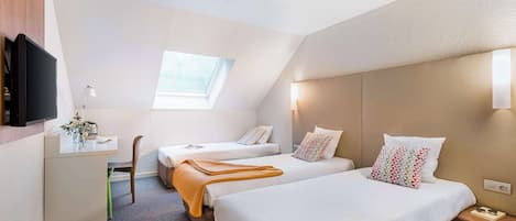 A hotel room with two beds, a desk, a TV, and a window.