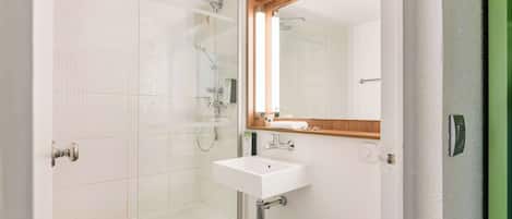 A bathroom with a glass shower enclosure, a white sink, and a mirror above it.