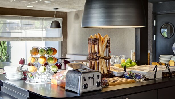A breakfast buffet setup with a toaster, fruit, bread, and condiments. - Campanile Geneve - Ferney-Voltaire (Ferney-Voltaire)
