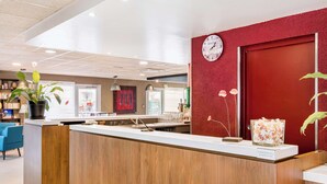 A reception area with a wooden counter, a clock, and a red wall. - Campanile Geneve - Ferney-Voltaire (Ferney-Voltaire)