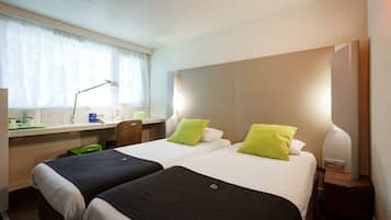 A hotel room with two beds, a desk, a chair, a lamp, and a window with curtains.