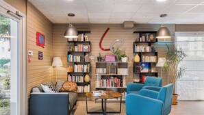 A modern lobby with a sofa, chairs, a coffee table, and bookshelves. - Campanile Geneve - Ferney-Voltaire (Ferney-Voltaire)