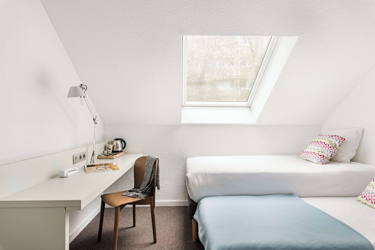 A small, modern room with a desk, chair, and two beds.