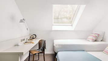 Une petite chambre moderne équipée d’un bureau, d’une chaise et de deux lits.