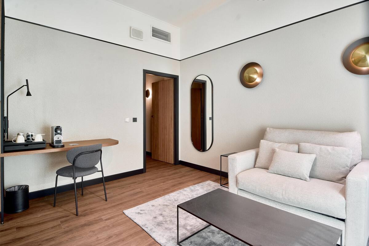 Een moderne woonkamer met een bank, een salontafel, een bureau met een stoel en een grote spiegel.