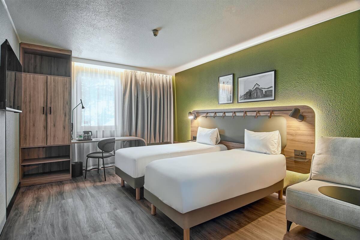 Een hotelkamer met twee bedden, een bureau, een stoel en een groene accentmuur.