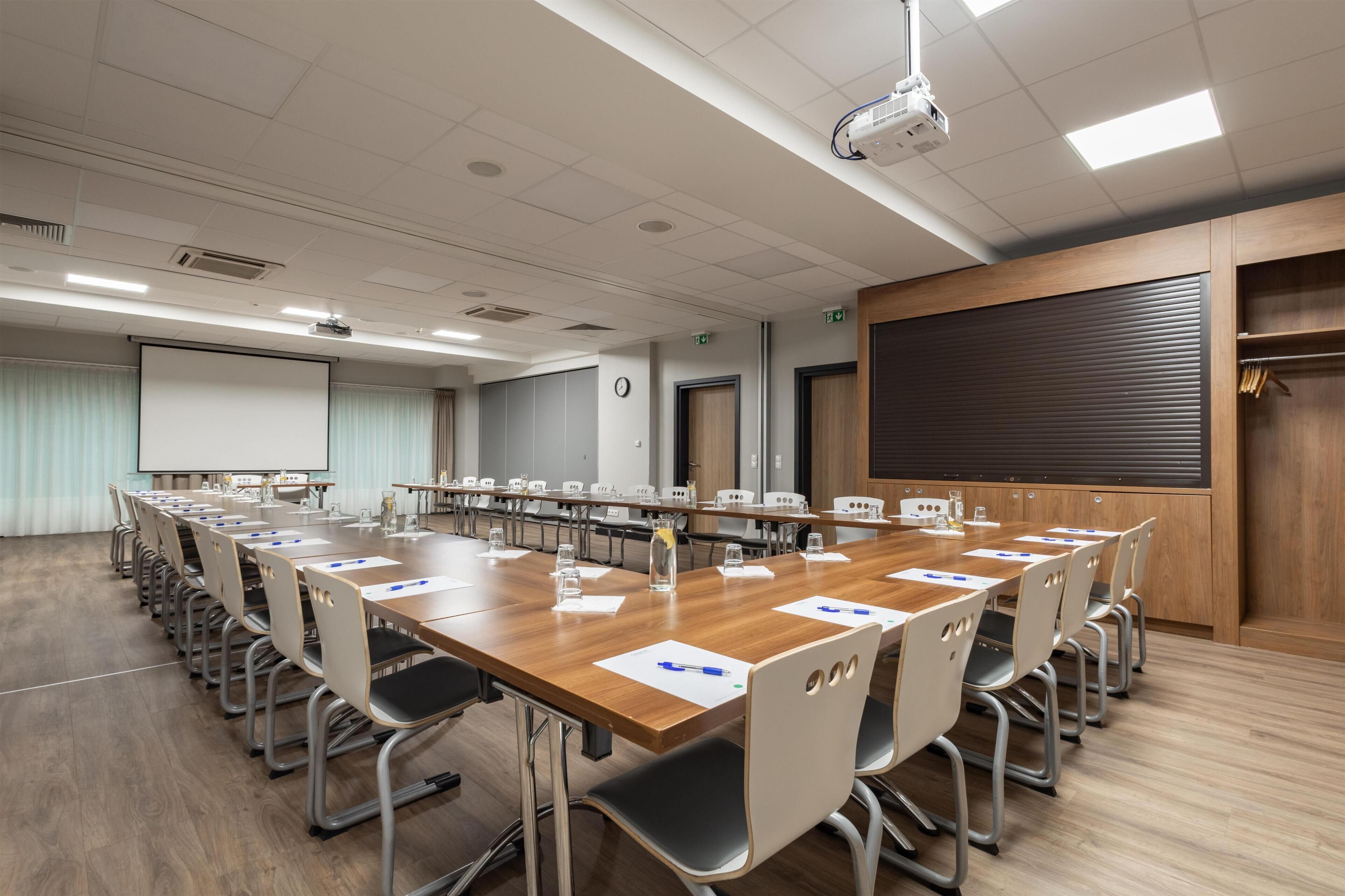 Ein Konferenzraum mit einem langen Tisch, Stühlen, einem Projektor und einer Leinwand.